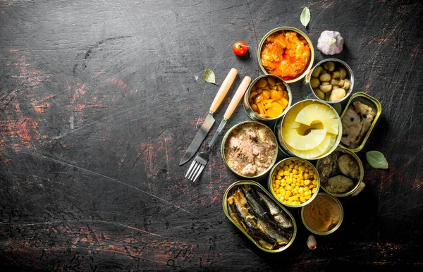 Konserve mantar, ananas, mısır, et ve balık açık konserve konserve. Koyu rustik arka plan üzerinde