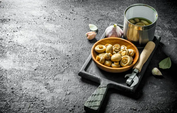 Sarımsak karanfil ve Defne yaprağı ile kesme Tahtası üzerinde Konserve mantar. Siyah rustik arka plan üzerinde