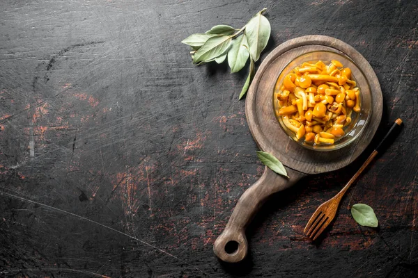 Stock image Pickled mushrooms in a glass bowl on a cutting Board. On dark rustic background