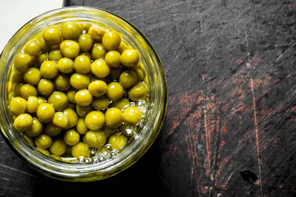 Cam kavanozda konserve yeşil bezelye. Koyu rustik arka plan üzerinde