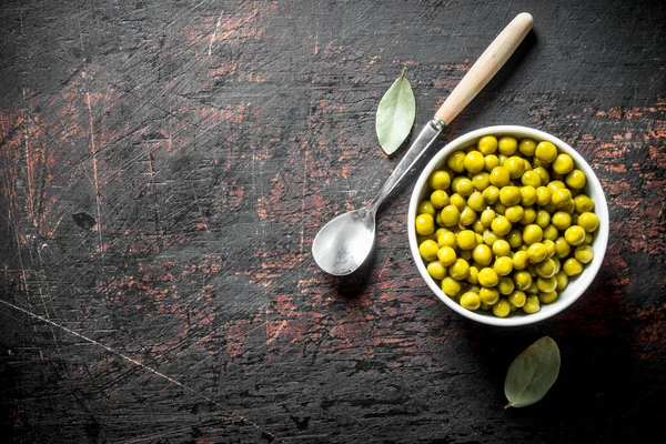 Kaşık ve Defne yaprağı ile kase de Konserve yeşil bezelye. Koyu rustik arka plan üzerinde