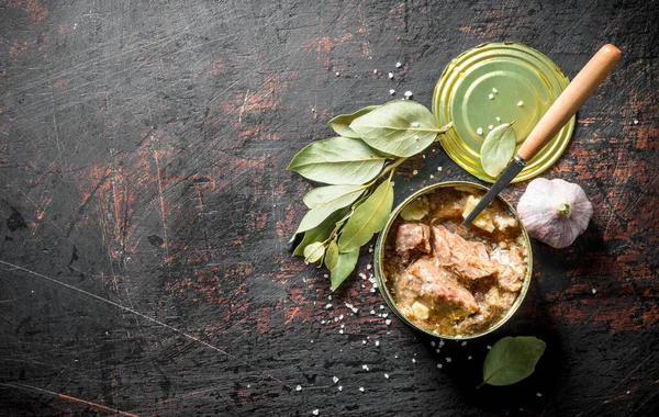 Bir kaşık, sarımsak ve Defne yaprağı ile bir teneke içinde konserve et. Koyu rustik arka plan üzerinde
