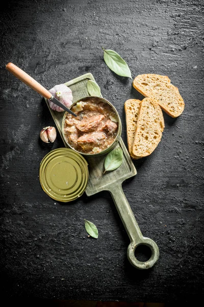 Ekmek ve sarımsak dilimleri ile kesme Tahtası üzerinde bir konserve et. Siyah rustik arka plan üzerinde