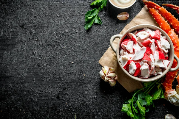 Yeşillik, sos ve sarımsak ile kağıt üzerinde kase de Yengeç eti. Siyah rustik arka plan üzerinde