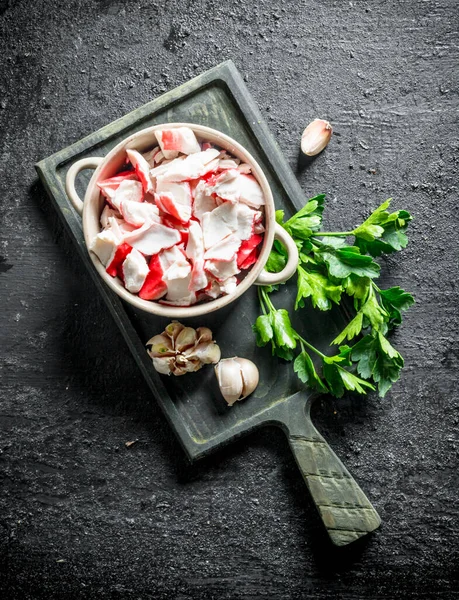 Maydanoz ve sarımsak karanfil ile kesme Tahtası üzerinde bir kapta Yengeç eti. Siyah rustik arka plan üzerinde