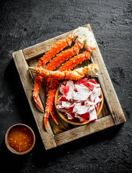 Yengeç eti ve taze yengeç, tahta tepside soslu. Siyah rustik arka plan üzerinde