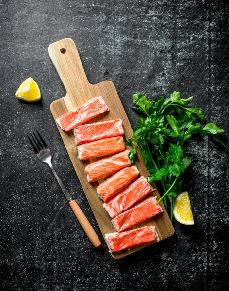 Yengeç maydanoz ve limon ile doğrama tahtası üzerinde sopalarla. Koyu rustik arka plan üzerinde