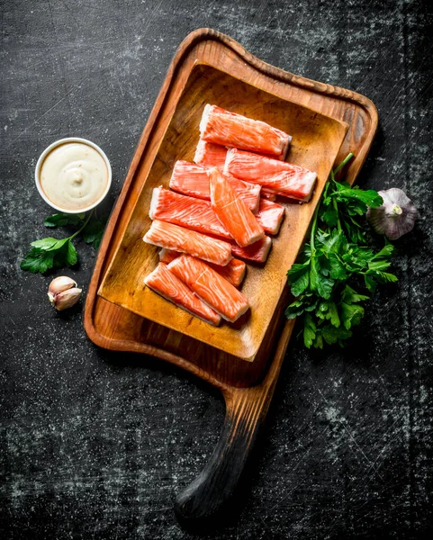 Yengeç yeşillik, sos ve sarımsak ile kesme Tahtası üzerinde sopalarla. Koyu rustik arka plan üzerinde