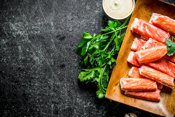 Yengeç yeşillik ve sos ile ahşap bir tabak üzerinde sopalarla. Koyu rustik arka plan üzerinde