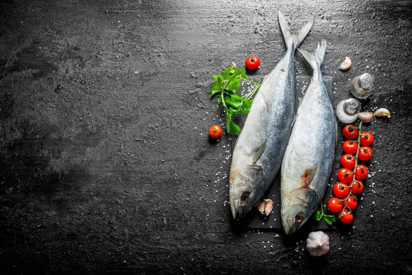 stock image Raw fish with spices, tomatoes and herbs. On black rustic background