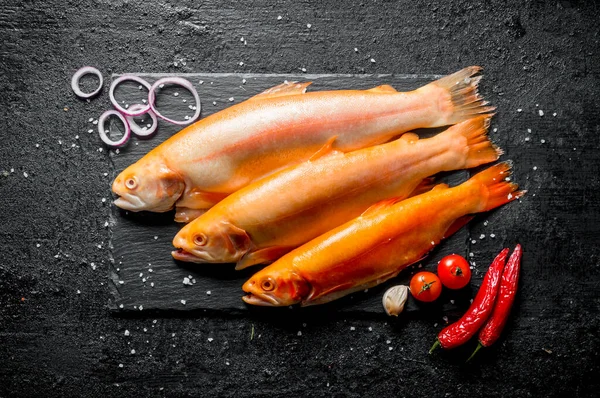 stock image Raw fish trout with chili pepper, tomatoes and onion rings. On black rustic background