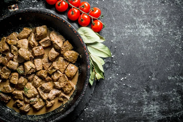 Stock image Fried liver in a pan with Bay leaf and tomatoes. On dark rustic background