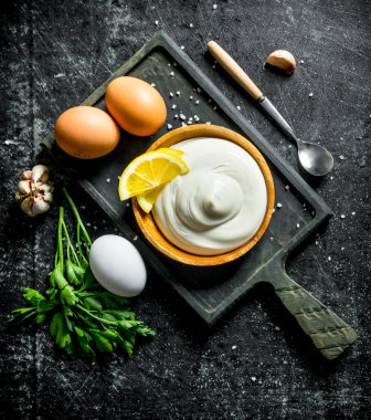 Yumurta, maydanoz, sarımsak ve limon dilimleri ile bir kesme Tahtası üzerinde Mayonez. Koyu rustik arka plan üzerinde