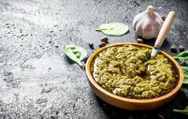 Kaşıkla tahta kasede pesto sosu. Siyah rustik arka plan üzerinde