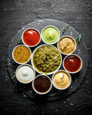 Pesto sosu, domates sosu, barbekü sosu, hardal, mayonez, bir taş tahta üzerinde guakomole sosu. Siyah rustik arka plan üzerinde