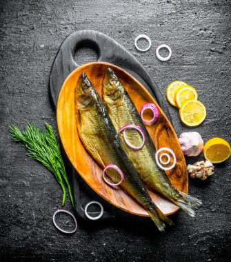 Dereotu ile füme balık, limon ve soğan dilimleri. Siyah rustik arka plan üzerinde