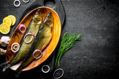 Dereotu ile füme balık, limon ve soğan dilimleri. Siyah rustik arka plan üzerinde