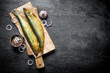 Soğan halkaları, baharatlar ve sarımsak ile kesme Tahtası üzerinde Füme balık. Siyah rustik arka plan üzerinde