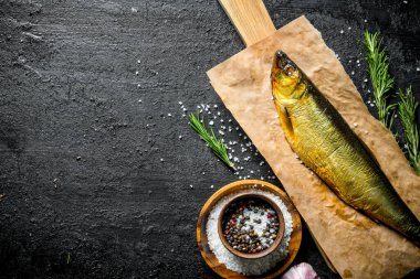 Baharat, biberiye ve sarımsak ile kağıt üzerinde füme balık. Siyah rustik arka plan üzerinde