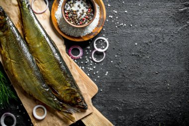 Baharat ve soğan halkaları ile kağıt üzerinde füme balık. Siyah rustik arka plan üzerinde