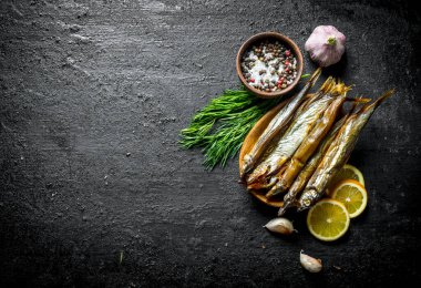 Limon dilimleri, dereotu, sarımsak ve baharat ile Füme balık. Siyah rustik arka plan üzerinde