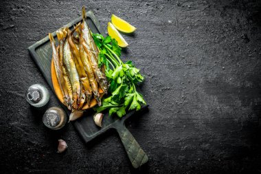 Maydanoz, baharat ve limon dilimleri ile kesme Tahtası üzerinde Füme balık. Siyah rustik arka plan üzerinde