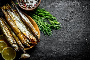 Otlar, limon ve baharatlar ile Füme balık. Siyah rustik arka plan üzerinde