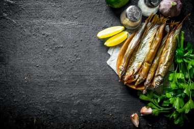 Limon dilimleri, otlar ve baharatlar ile Füme balık. Siyah rustik arka plan üzerinde