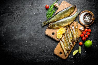 Limon dilimleri ile füme balık türleri, limon, domates ve otlar. Siyah rustik arka plan üzerinde