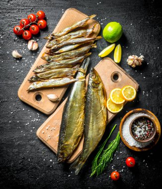 Füme ringa balığı ve limon, domates ve kireç ile sprat. Siyah rustik arka plan üzerinde