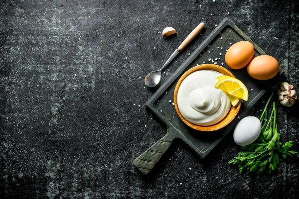 Yumurta, maydanoz, sarımsak ve limon dilimleri ile bir kesme Tahtası üzerinde Mayonez. Koyu rustik arka plan üzerinde