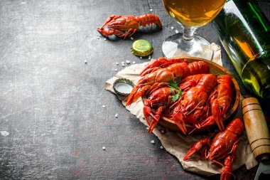 Bir bardak ve şişe de bira ile kağıt üzerinde bir tabakta kırmızı haşlanmış kerevit. Koyu rustik arka plan üzerinde