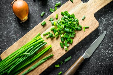 Bir bıçak ve soğan ile kesme Tahtası üzerinde doğranmış yeşil soğan. Koyu rustik arka plan üzerinde