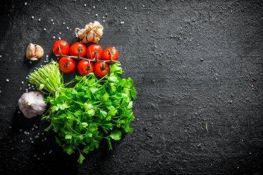 Kiraz domates ve sarımsak karanfil ile maydanoz demet. Siyah rustik arka plan üzerinde