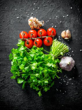 Kiraz domates ve sarımsak karanfil ile maydanoz demet. Siyah rustik arka plan üzerinde