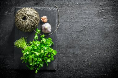 Sarımsak ve ip ile bir taş tahta üzerinde taze maydanoz. Siyah rustik arka plan üzerinde