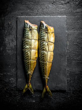 Taş bir tahtada tütsülenmiş uskumru. Siyah rustik arka plan üzerinde