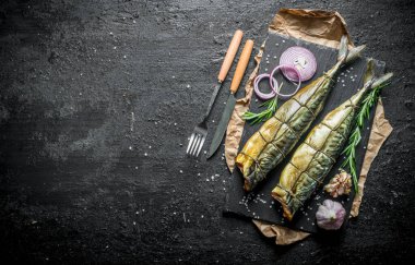 Taze soğan ve sarımsak karanfil halkaları ile lezzetli füme uskumru balık. Siyah rustik arka plan üzerinde