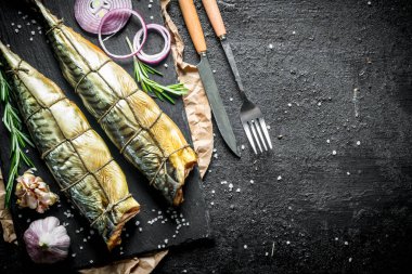 Taze soğan ve sarımsak karanfil halkaları ile lezzetli füme uskumru balık. Siyah rustik arka plan üzerinde