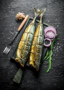 Kokulu doğranmış soğan, biberiye ve sarımsak bir prig ile uskumru füme. Siyah rustik arka plan üzerinde