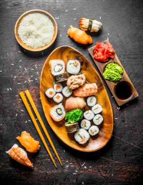 Suşi ve bir kase ve yemek çubukları haşlanmış pirinç ile bir tabak tabakta rulo. Koyu rustik arka plan üzerinde