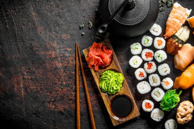 Japon suşi, rulo ve sos, wasabi ve yeşil çay bir çaydanlık ile maki farklı türleri. Koyu rustik arka plan üzerinde