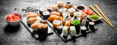 Yemek çubukları ile farklı suşi rulo. Siyah rustik arka plan üzerinde