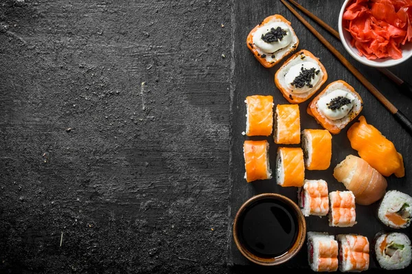 stock image Traditional Japanese sushi rolls with ginger and soy sauce on a black stone Board. On black rustic background