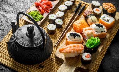 Yeşil çay ile bir peçete üzerinde suşi rulo seti. Siyah rustik arka plan üzerinde