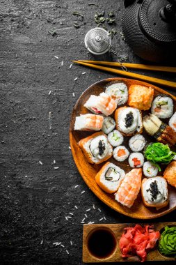 Taze suşi ve soslar ve yeşil çay ile rulo. Siyah rustik arka plan üzerinde