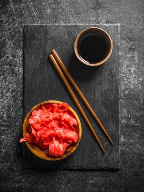 Soya sosu ve yemek çubukları ile bir taş Tahta üzerinde marine zencefil. Koyu rustik arka plan üzerinde