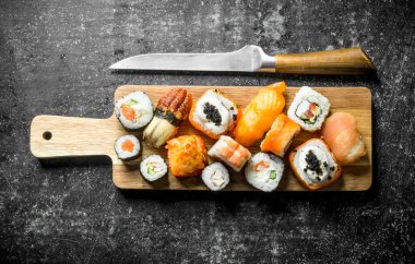 Bıçak ile ahşap kesme Kurulu çeşitli Japon suşi rulo. Koyu rustik arka plan üzerinde