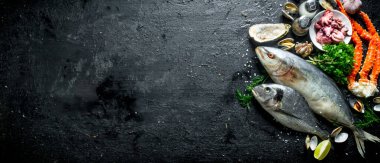 Deniz ürünleri. Taze balık, bebek ahtapotlar, yengeç, sarımsak, otlar ve kireç ile istiridye. Siyah rustik arka plan üzerinde