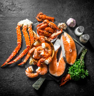 Haşlanmış karides, yengeç ve kerevit ile çiğ somon biftek. Siyah rustik arka plan üzerinde